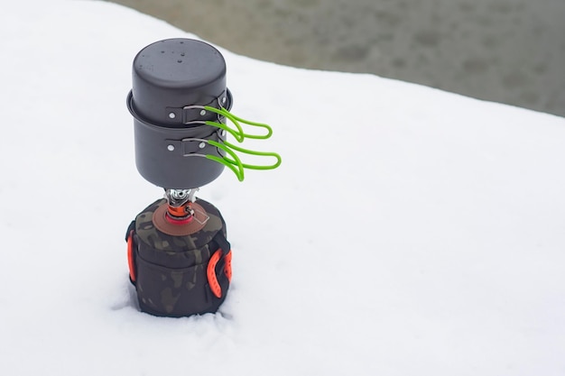 Winter camping in the open air against the backdrop of snow and lake Tourist gas burner with pans for cooking