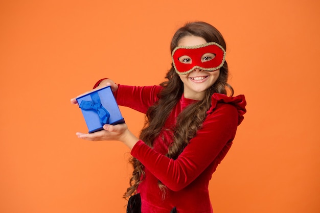 Winter carnival. Secret Santa gift concept. Kid wear eye mask. Girl in mask orange background. Winter event and entertainment. Child development. Visit public event anonymously. Winter new year party.