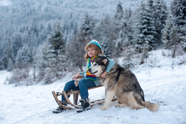 Winter child little boy having fun with husky dog in the snow