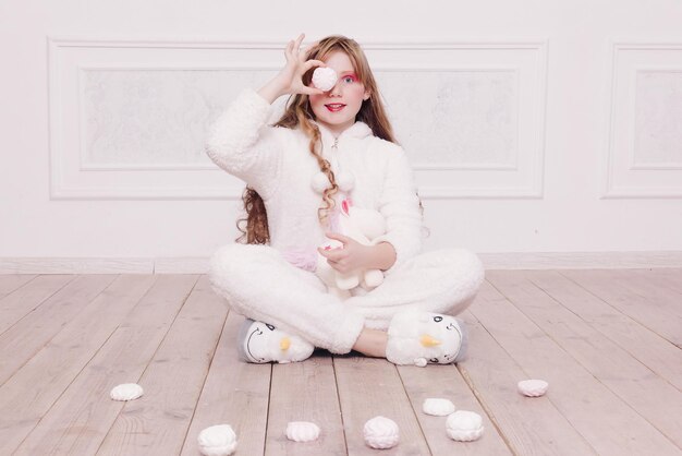 写真 冬、クリスマス、休日、お菓子、誕生日、お祝い、子供たちのコンセプト-床に座っているお菓子を持つかわいい女の子のパジャマ、幸せな子供時代のコンセプト。女の子の贈り物、柔らかい犬、シャボン玉。