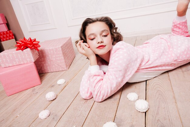 Winter, christmas, holiday, sweets, birthday, celebration and children concept- cute little girl pajama with sweets sitting on the floor, happy childhood concept. girl gifts, soft dog, soap bubbles.