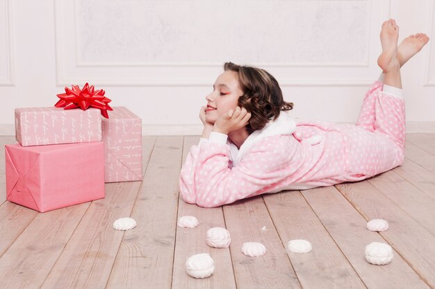 冬、クリスマス、休日、お菓子、誕生日、お祝い、子供たちのコンセプト-床に座っているお菓子を持つかわいい女の子のパジャマ、幸せな子供時代のコンセプト。女の子の贈り物、柔らかい犬、シャボン玉。