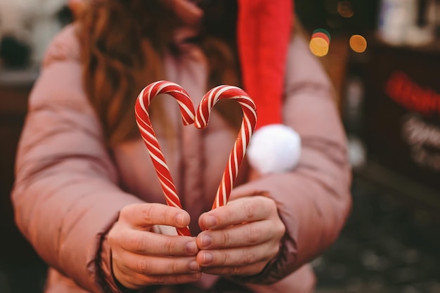 冬のクリスマスマーケットでは、女性の手がキャンディーから折りたたまれたハートのシンボルを持っています