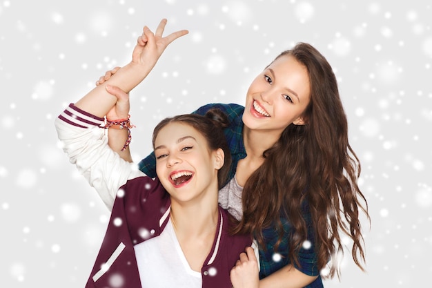 winter, christmas, people, teens and friendship concept - happy smiling pretty teenage girls or friends showing peace hand sign over gray background and snow