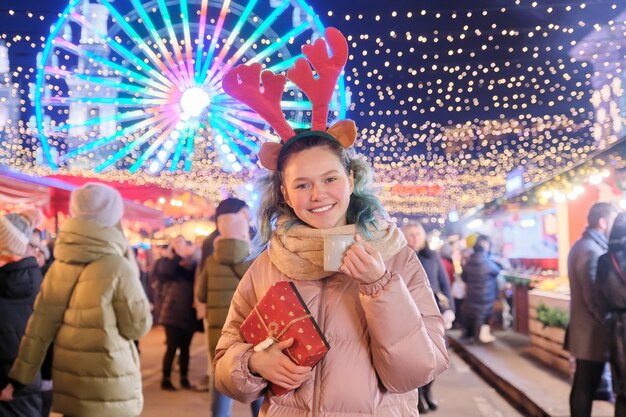 Winter Christmas portrait of happy teenage girl with gift box at holiday outdoor city market