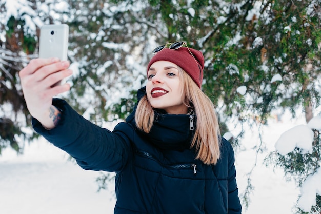 Winter, christmas, technologies, people, lifestyle and beauty concept -SELFI TIME. Pretty brunette girl doing a selfie with her smart phone.Beautiful young woman. Outdoor winter portrait.