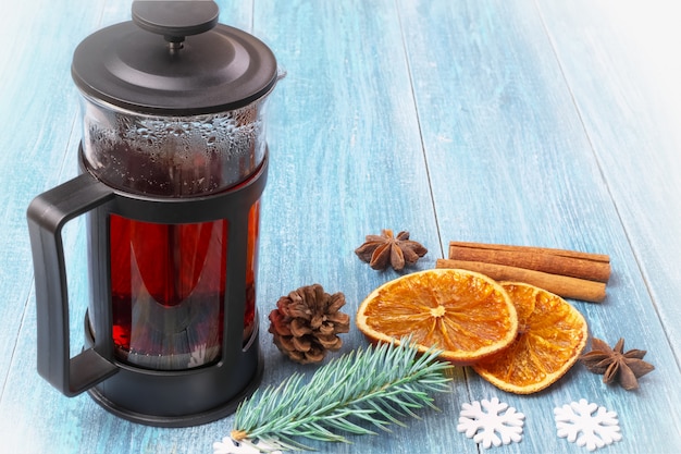 Winter Christmas vintage still life: a French press with black tea, tangerines, dried oranges, cinnamon sticks and anise stars on a textured, blue wooden surface