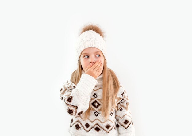 겨울옷. 하얀 겨울 모자를 쓴 곱슬머리 소녀의 초상화. 흰색 니트 모자와 스웨터 웃는 밝은 배경 분리에 작은 금발 소녀