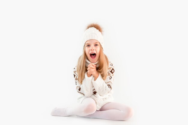 Winter clothes. Portrait of a little curly-haired girl in a knitted white winter hat. little blonde girl in white knitted hat and sweater smiling light background isolate