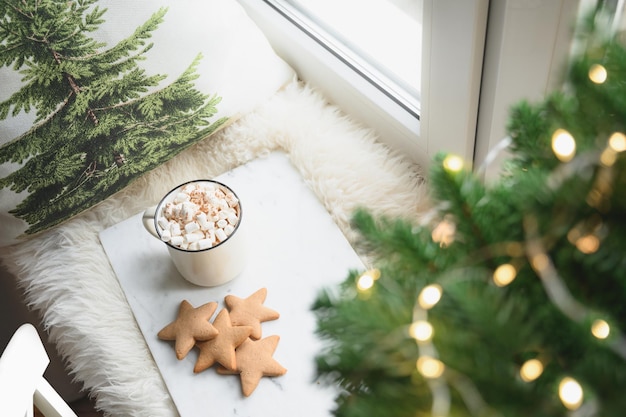 Winter coffee with marshmallow on cozy window sill with christmas tree