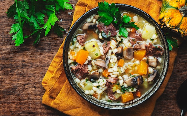 Winter comfort food Warming soup with pumpkin mushrooms vegetables beef and barley Rustic wooden table background top view