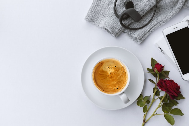 Winter concept. cup of coffee, smartphone, rose flower and sweater on white table background. top view