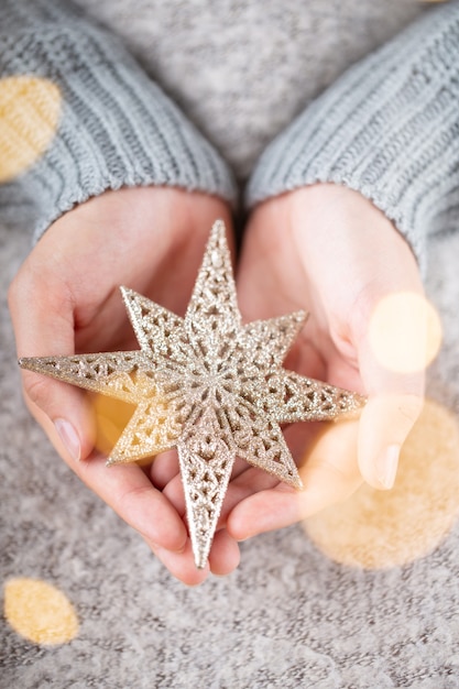 冬のコンセプト若い手がクリスマスの装飾を保持しています。クリスマスの装飾のアイデア。女性の手にクリスマスの装飾、金のボケ味の背景。