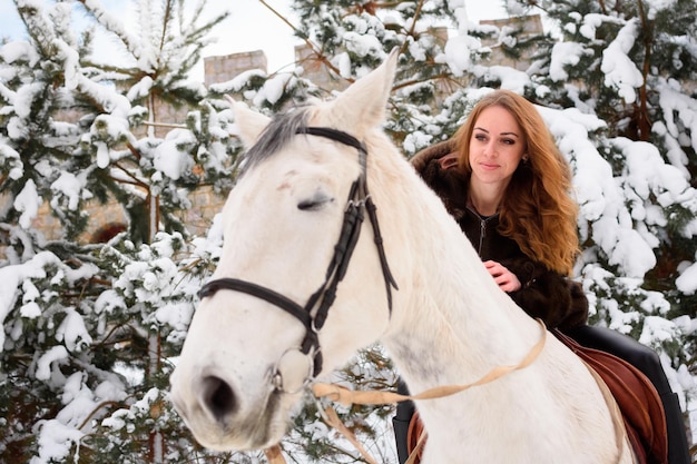 Winter coniferous forest with snow a young girl with long hair\
in a fur coat riding a horse