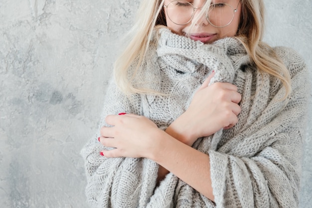 Winter coziness. Peaceful, smiling woman in gray knitted blanket.