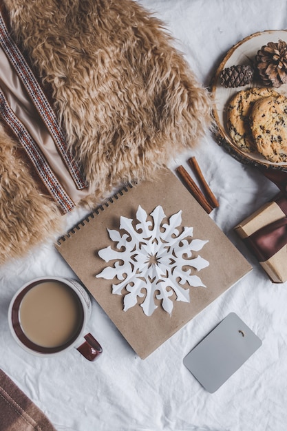 Foto inverno accogliente. pelliccia, plaid, quaderno, tazza di caffè, biscotti, caramelle al cioccolato sul letto