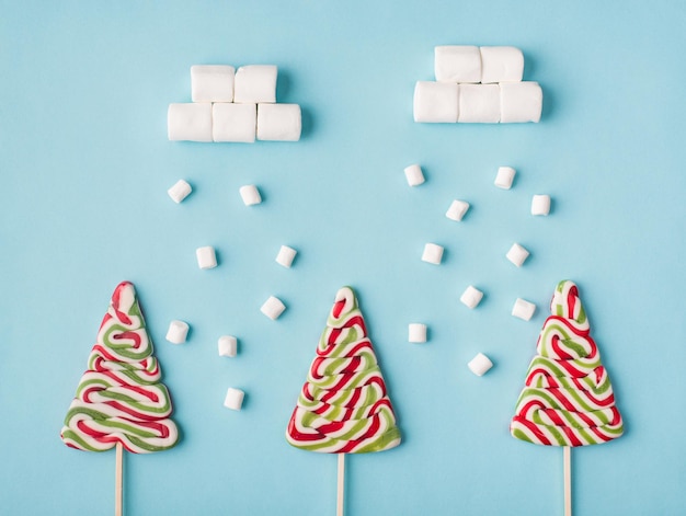 Foto concetto di composizione dolce creativa invernale. tre alberi di caramello duro e neve di marshmallow che cade su uno sfondo di colore morbido pastello