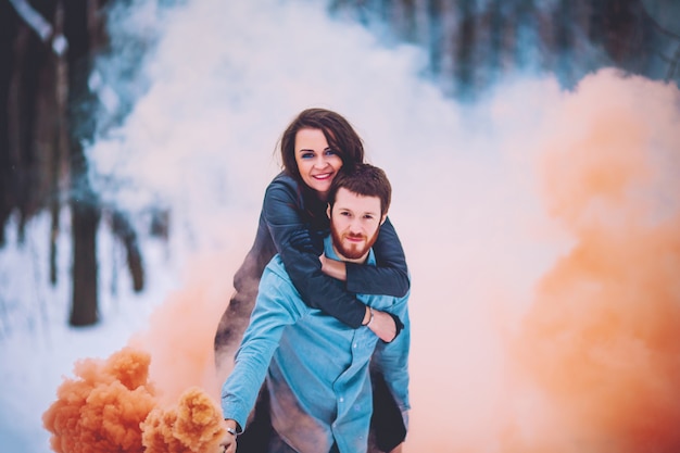 Winter and date. Young couple in love with man and woman in the winter against background of snow covered trees in park are embrace. A guy with long hair and beard keeps skates and loves girlfriend.