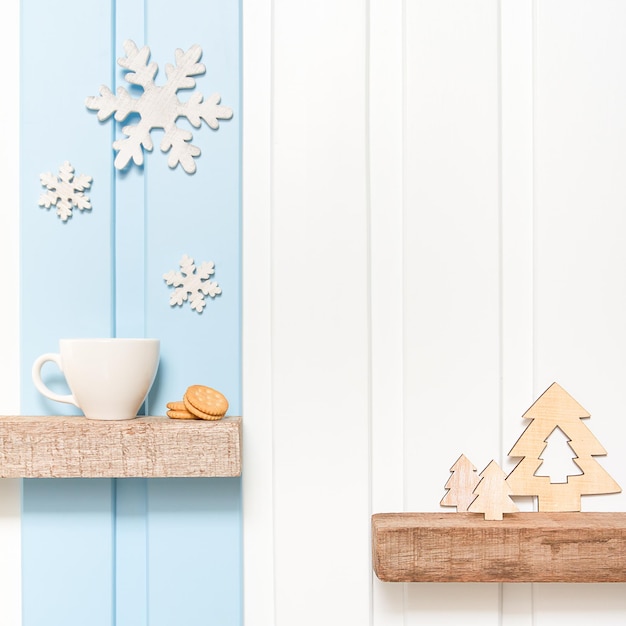 Winter decorations background Coffee cup with wooden snow flake pines on shelf over blue white wall