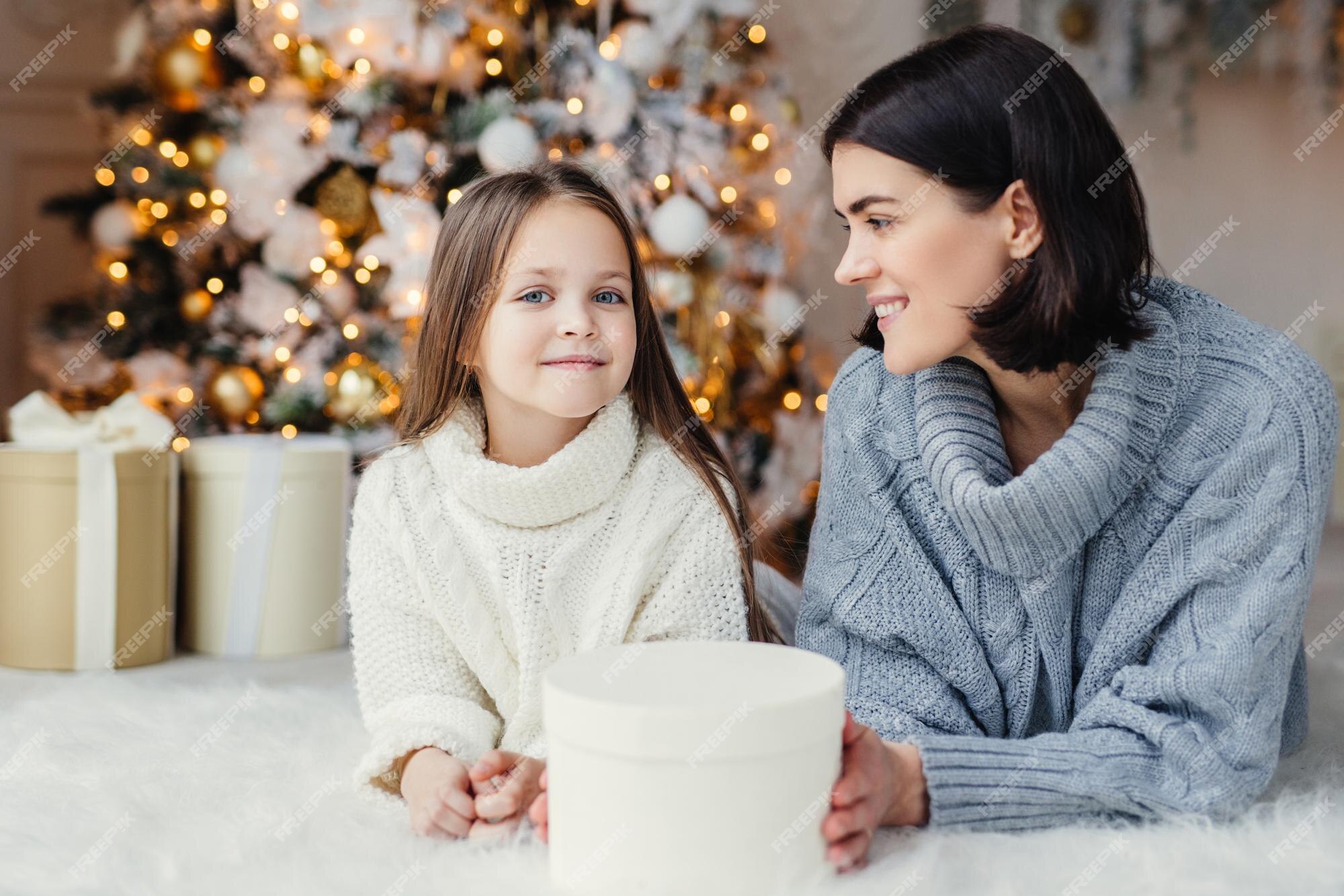 Winter en viering concept vrij mooi blauwogig klein vrouwelijk kind in gebreide witte trui en brunette vrouw hebben goede rust thuis tijd doorbrengen in de buurt van kerstboom | Premium Foto