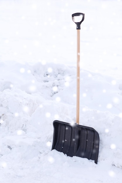 winter and equipment concept - black snowshowel with wooden handle in snow pile