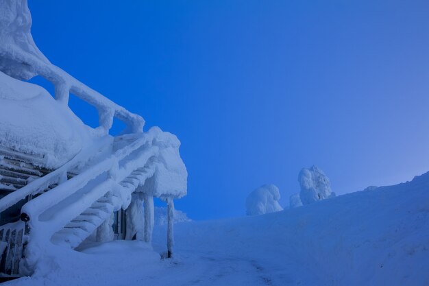 Winter evening at a ski resort. Snow-covered stairs of the cafe. A lot of snow