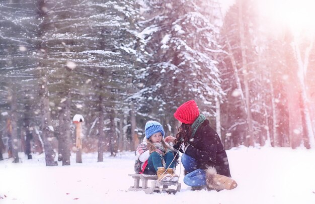 Winter fairy tale a young mother and her daughter ride a sled in the forest