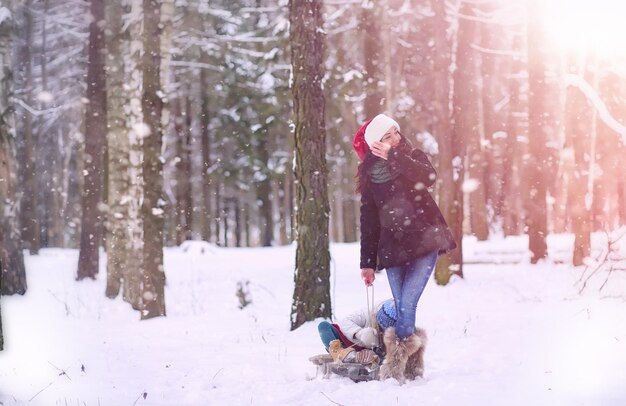 Winter fairy tale a young mother and her daughter ride a sled in the forest