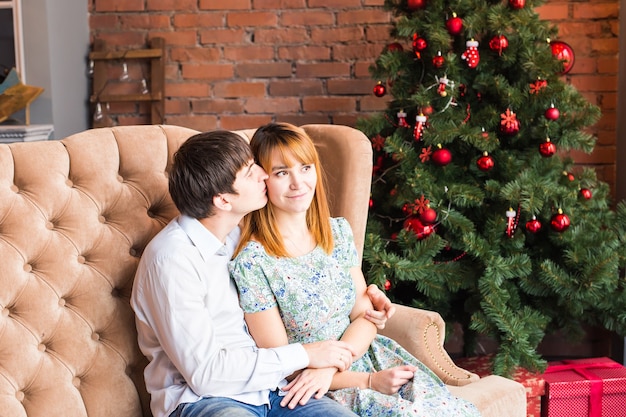 Winter, fashion, couple, christmas and people concept - smiling man and woman hugging over christmas tree
