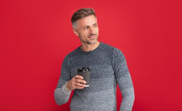 Winter fashion morning coffee glad grizzled guy in sweater on red background