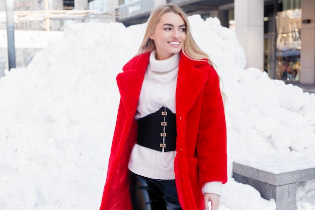 Winter, fashion, people concept - fashion Portrait of a beautiful young woman walks around the city smiling red fur coat close-up snowflakes cold winter, breathe fresh air at frost winter day. sunset