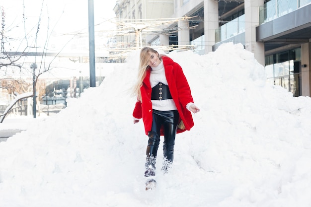 冬、ファッション、人々のコンセプト-ファッション美しい若い女性の肖像画は、赤い毛皮のコートのクローズアップ雪片の寒い冬を笑顔で街を歩き、霜の冬の日に新鮮な空気を吸います。日没