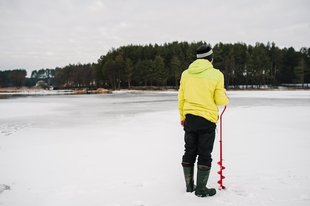 Зимний рыбак бурит лунку ледобуром Рыбак бурит бур на замерзшем озере Зимняя рыбалка на пруду