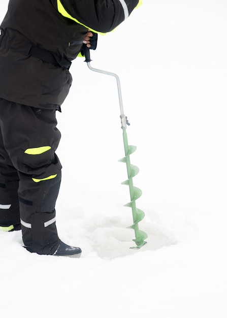 Winter fishing on ice. Man drilling a hole in the ice. Relaxing in the wild