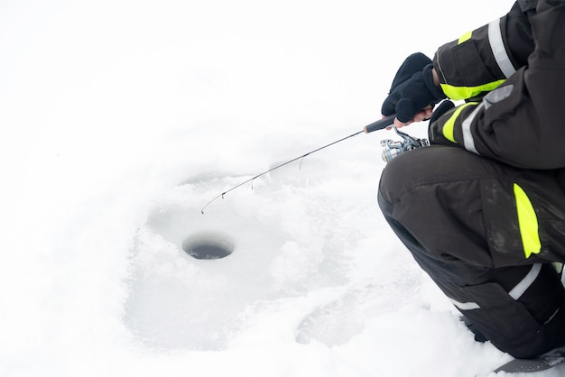 Pesca invernale sul ghiaccio. l'uomo jiggling esca in un buco nel ghiaccio.