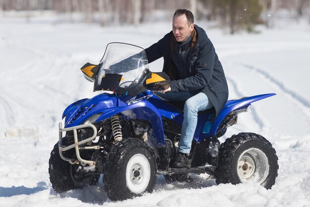 A winter forest in daylight cold weather an adult man riding a big blue snowmobile