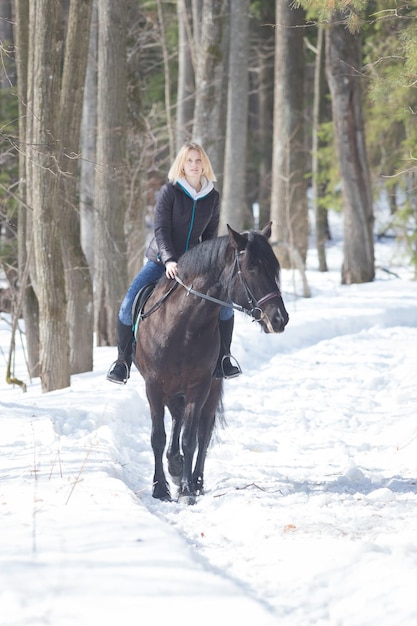 A winter forest a young woman riding a black horse