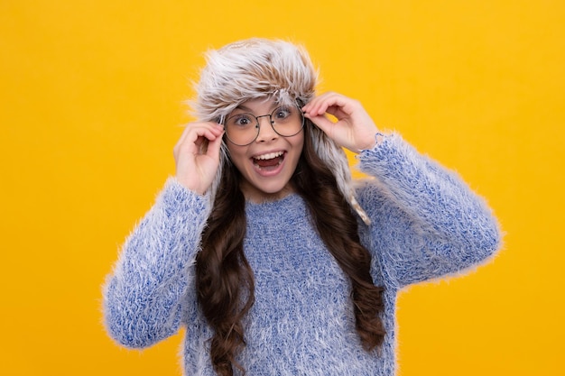 Cappello invernale concetto di stagione fredda accessorio moda invernale per bambini ragazza teenager che indossa un caldo cappello lavorato a maglia viso eccitato emozioni allegre di una ragazza adolescente