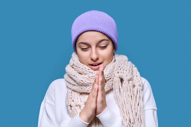 Winter headshot portrait of young female in hat sweater scarf Happy beautiful cute teenage girl on blue studio background Cold season New Year Christmas holidays fashion beauty concept