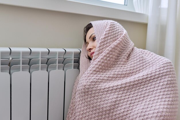 Winter heating season Woman in warm sweater sitting in home room near heating radiator