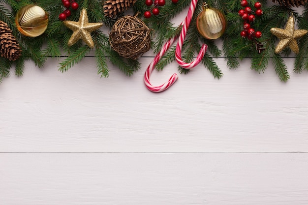 Winter holiday background. Green fir branches with decorations and lollipops on white wooden table, top view, copy space