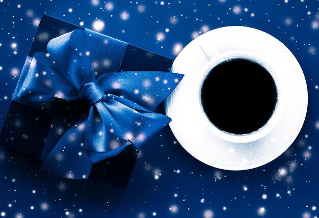 Foto confezione regalo per le vacanze invernali tazza da caffè e neve incandescente su sfondo blu flatlay sorpresa del regalo di natale