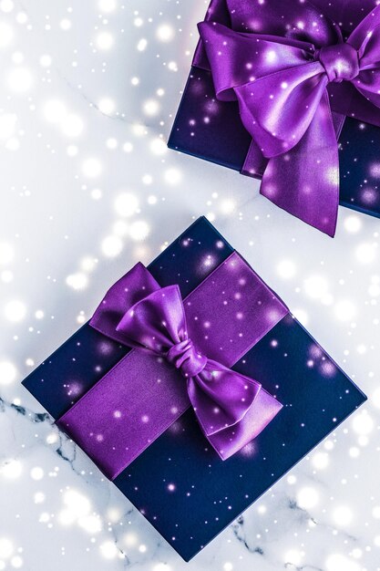 Winter holiday gift box with purple silk bow snow glitter on marble background as Christmas and New Years presents for luxury beauty brand flatlay design