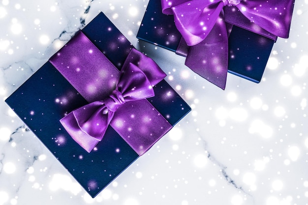 Photo winter holiday gift box with purple silk bow snow glitter on marble background as christmas and new years presents for luxury beauty brand flatlay design