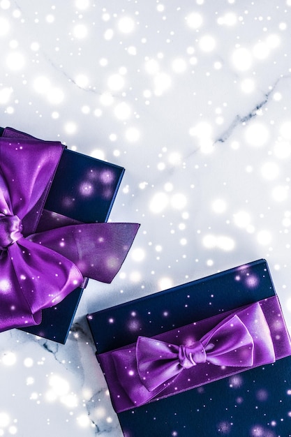 Foto confezione regalo per le vacanze invernali con fiocco di seta viola con glitter di neve su sfondo marmoreo come regali di natale e capodanno per un design flatlay di lusso di marca di bellezza