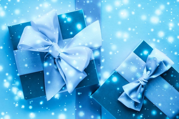 Winter holiday gifts and glowing snow on frozen blue background Christmas presents surprise