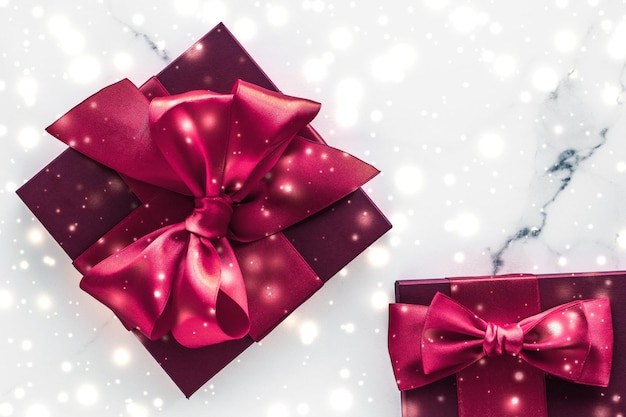 Winter holiday gifts with cherry silk bow and glowing snow on frozen marble background Christmas presents surprise