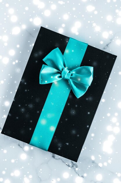 Winter holiday gifts with emerald silk bow and glowing snow on frozen marble background christmas presents surprise