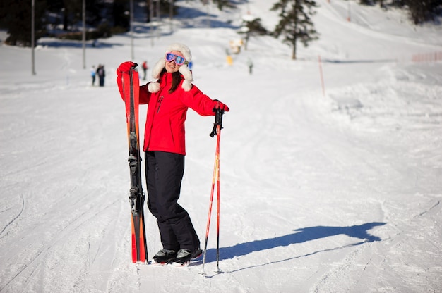 Winter holiday and sport concept with woman with skis in her hands at the foot of the mountain