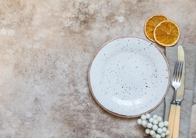 Winter holiday table setting Craft ceramic plate linen napkin cutlery and dry oranges slices